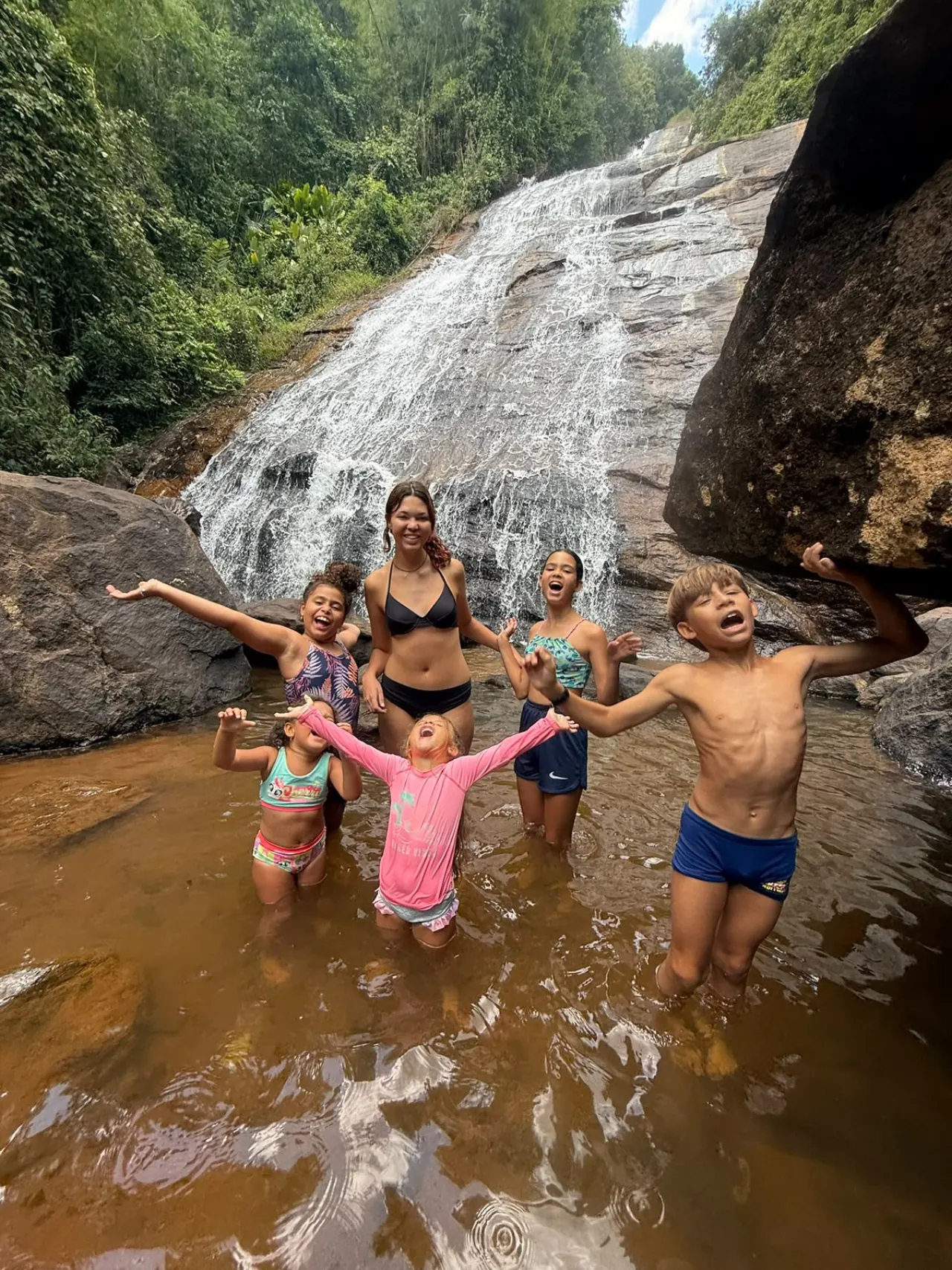 Crianças se divertindo no riacho diante da cachoeira